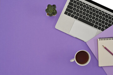 Top view with modern laptop computer, coffee cup and notebook on purple background, Copy space.