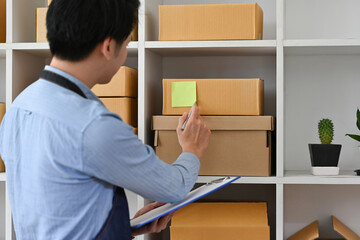 An employee man use document checklist checking stock goods supply, delivery package shipping, product purchase order.