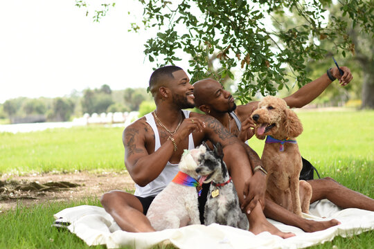 USA, Louisiana, Smiling gay couple with dogs taking selfie on lawn in park