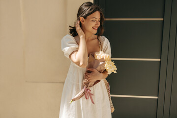 Pretty young caucasian woman modestly looks away relaxing outdoors. Brunette wears white sundress...
