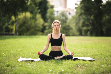 Young woman in lotus position practicing yoga outdoors in city park
