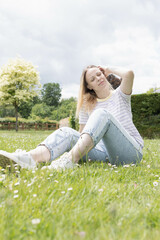 a girl with blond hair of European appearance sits in a park on green grass