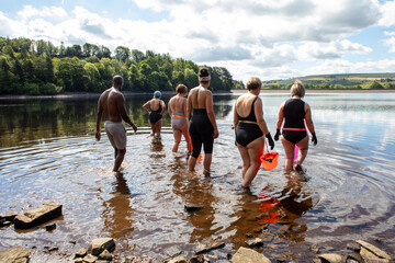 Rear view of group of friends entering lake, Yorkshire, UK - obrazy, fototapety, plakaty