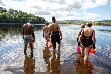 Rear view of group of friends entering lake, Yorkshire, UK