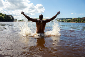 Rear view of man splashing water in lake, Yorkshire, UK