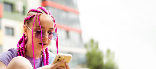 Portrait of a caucasian teenage hipster girl with pink braids using a smartphone on a street...