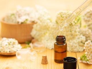 Bottle of essential oil with fresh flowering yarrow branches in the background on a wooden table .alternative medicine