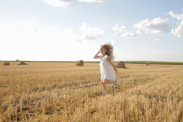 Fototapeta na wymiar Adorable little girl in white dress in a wheat field