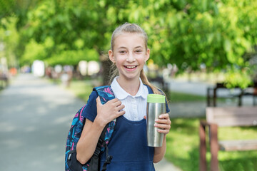 Smiling schoolgirl preteen goes to school with backpack and drink. Concept of back to school