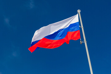 National flag of Russia is waving on white pole under blue sky