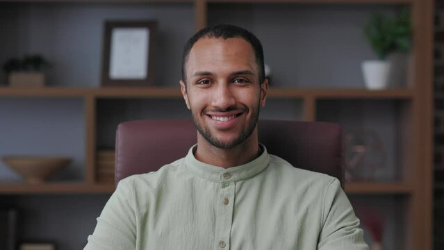 Close up business portrait of confident handsome mixed race man looking at camera and smiling. Young modern male leader, entrepreneur, manager indoors at workplace in office. Successful businessman.