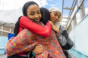 Young women wearing hijabs hugging in city - obrazy, fototapety, plakaty