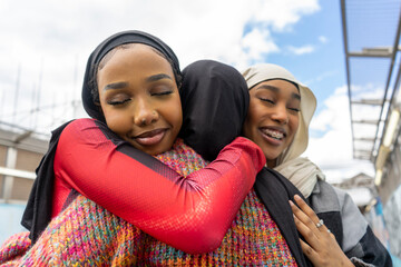 Young women wearing�hijabs�hugging in city - obrazy, fototapety, plakaty