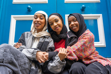 Portrait of three smiling women wearing hijabs embracing in city