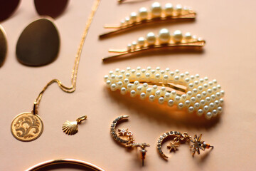 Various gold jewelry and pearl hair clips on peach colored background. Selective focus.