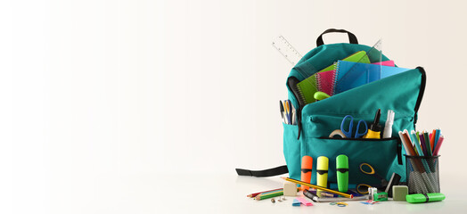 Blue school backpack full of school supplies on white table
