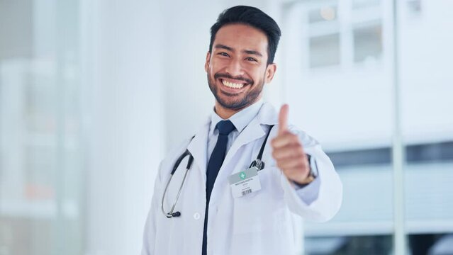 Male medical professional showing a sign of approval and symbol of agreement and trust. Doctor giving thumbs up hand gesture while smiling and looking confident, standing inside a hospital.