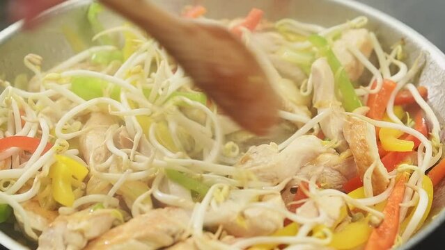 Cooking of stir fry chicken with bell peppers in a frying pan.
