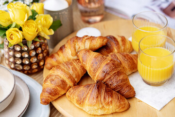 freshly baked homemade croissants with orange juice for breakfast on a table with yellow roses