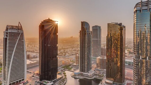 Sunrise over tall residential buildings at JLT district aerial timelapse, part of the Dubai multi commodities centre mixed-use district. Skyscrapers around pond