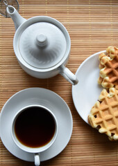 Tea couple with Viennese waffles on a mat. Tea party with waffles. A porcelain cup and saucer on a mat.