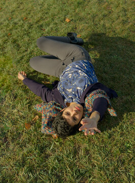 full length image of a short haired woman lying down on the grass looking and pointing at camera with her left hand