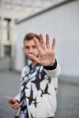 A handsome man in a white and black suit hides from the paparazzi and sticks out his hand. Guy with stubble and a model hairstyle in a fashionable suit sticks out his hand so as not to be filmed.