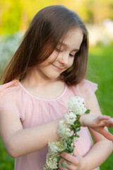 Portrait of a tender girl who admires a bracelet of natural  flowers dressed in a pink dress, with loose hair,  in the spring park