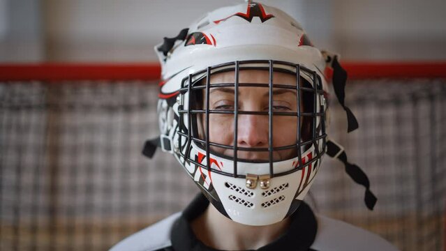 Close-up of woman floorball goalkeeper putting on helmet and preapring for game in gym.