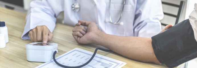 Male doctor uses a blood pressure monitor to check the body pressure and pulse of the patients who come to the hospital for check-ups, Medical treatment and health care concept.