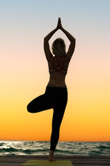 Fototapeta na wymiar A young woman practices yoga on the ocean coast during sunrise.