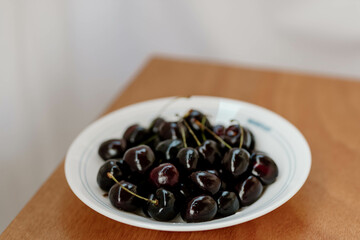 Fresh dark black very big huge sweet cherries and water drops on plate on wooden table background, close up. High quality photo of freshly picked organic fruit to eat. Summer harvest. Selective focus