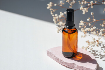 Amber pump bottle with serum, tonic or essential oil on pink concrete podium. White background with daylight with wild flowers. Beauty concept for face and body care