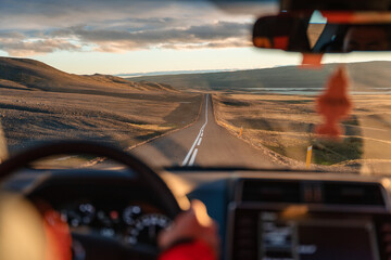 Man driving a car through wilderness on asphalt road in the sunset