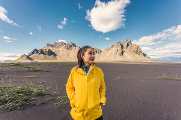 Young asian woman in yellow jacket standing on the beach with Vestrahorn mountain in viking village on Stokknes at Iceland