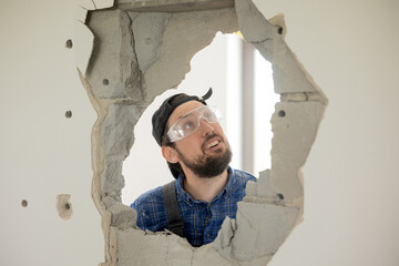 The man looks in shock at the hole he has punched in the wall with a hammer. Hopeless builder weak...
