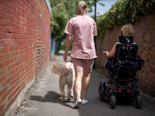 Woman in electric wheelchair going on walk with dog and assistant