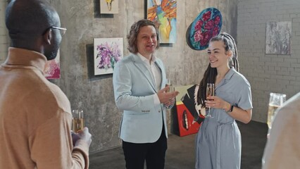 Medium long of artists and business people holding glasses with sparkling wine, celebrating opening of modern art gallery