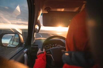 Fototapeta premium Man driving a car through wilderness on asphalt road in the sunset