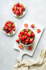 Fresh ripe strawberries in white bowl on white cutting board on rustic table, red summer fruit