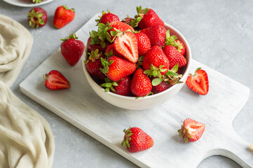 Fresh ripe strawberries in white bowl on white cutting board on rustic table, red summer fruit