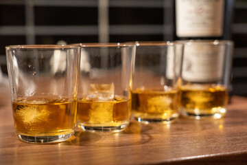 Whiskey glasses on a table, half filled with whiskey bottle blurred in the background 