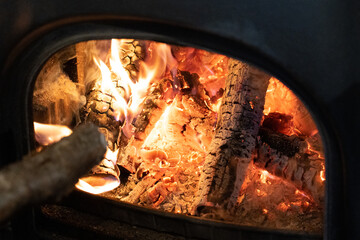 Putting more wood into an orange firer burning in a stove, embers glowing 