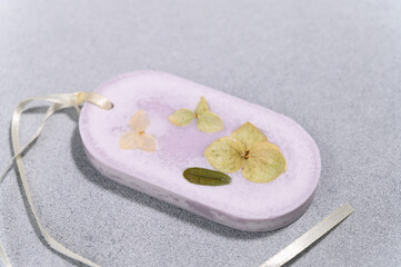 Closeup Lilac Soy Wax Oval Shape Sachet with Yellow Dried Flowers on Concrete Plank.