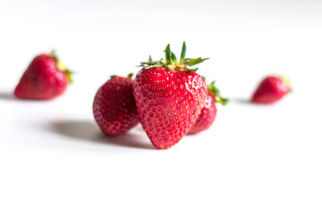 Three strawberries close-up on a light background. Main strawberry in focus and others in the background in strong defocus