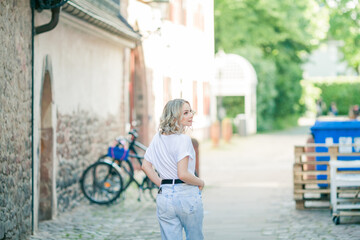 Fototapeta na wymiar Young beautiful blue-eyed blonde in the center of a European city. Portrait of a stylish model in casual clothes. Happy youth.
