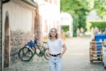 Young beautiful blue-eyed blonde in the center of a European city. Portrait of a stylish model in casual clothes. Happy youth.