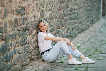 Young beautiful blue-eyed blonde in the center of a European city. Portrait of a stylish model in casual clothes. Happy youth.