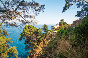 Scenic view of the white lighthouse, which stands on a mountain hill surrounded by trees near the azure sea