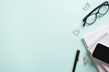 Smartphone, clean blank notepad, glasses, pen, paper clips, pencil on a light blue background. Make room for the text. Blogging in the workplace is a business. Copy space. Flat lay, top view